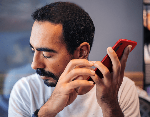 A man intently listening to his red phone with his eyes closed.